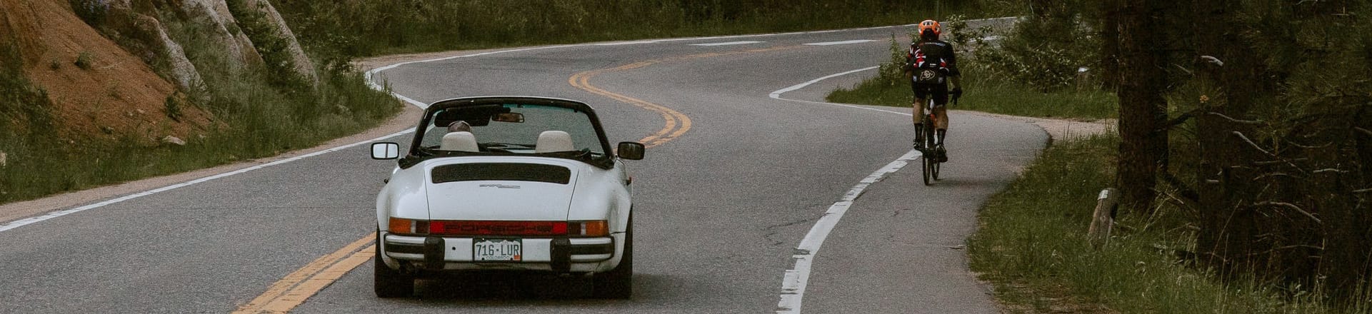 A sports car and a bicyclist on a winding road.