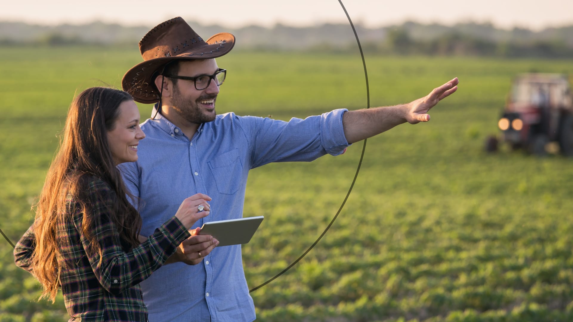 Woman and man pointing in field and tractor in the background