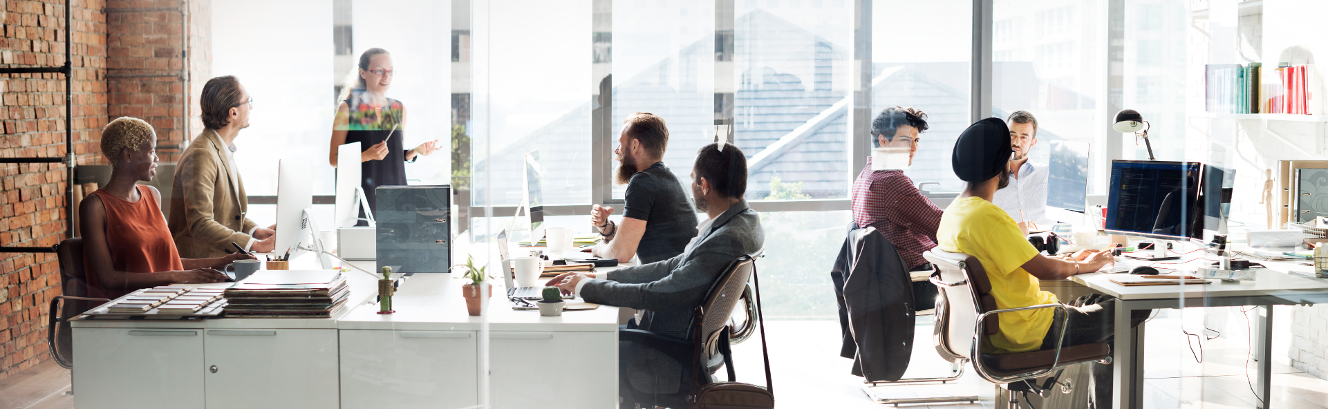 A group of young people working in an open office in front of windows