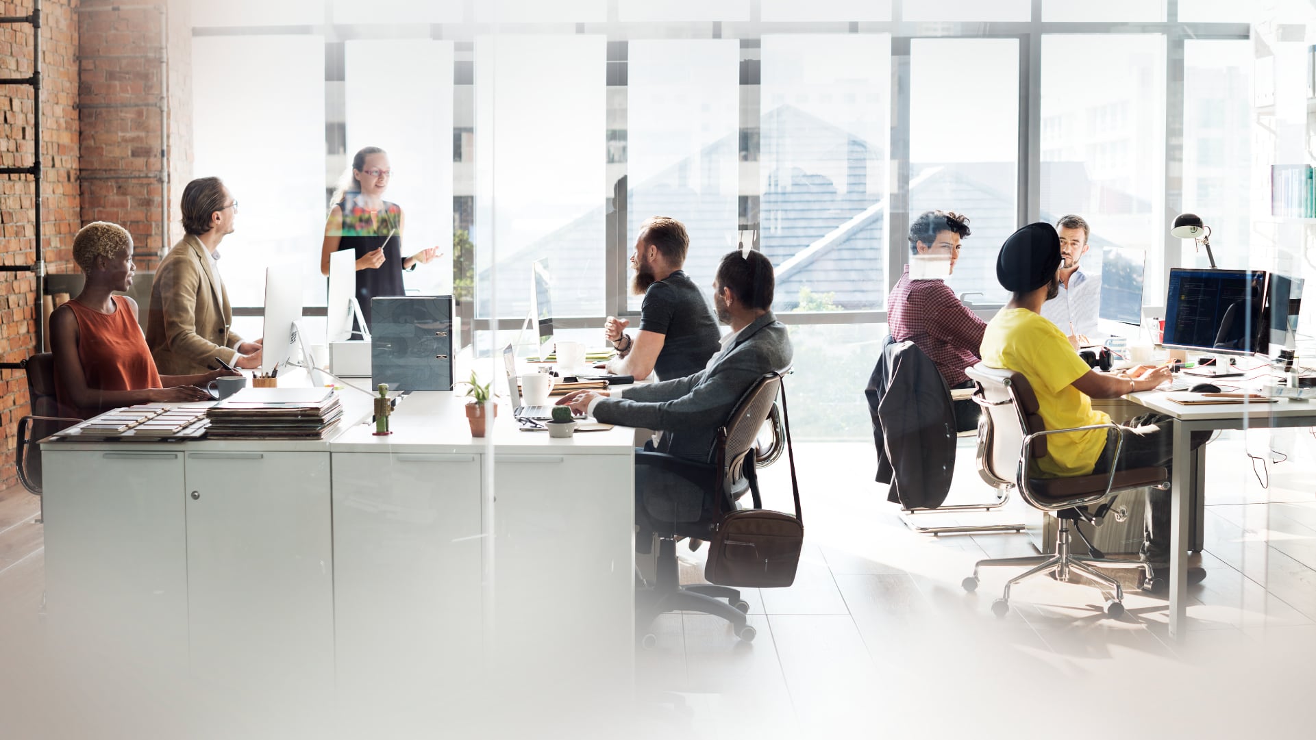 A group of young people working in an open office in front of windows